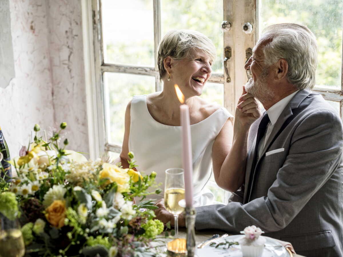 Couple marié souriant à table avec champagne et fleurs, célébrant leurs 29 ans de mariage lors des noces de velours